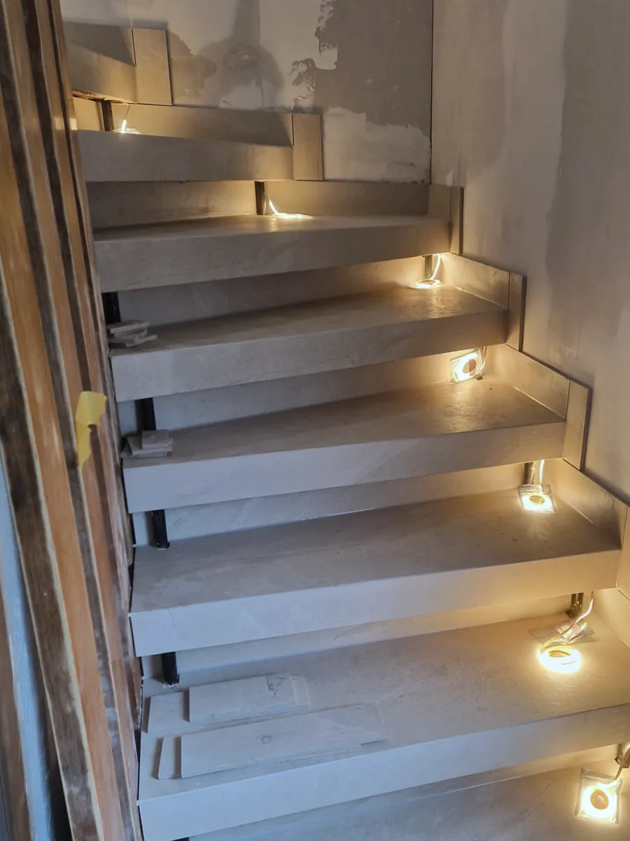 Dieselbe Treppe nach dem Umbau: Stufen neu belegt, an der Wand ein gefliester Sockel, an jeder Stufe ein warmes Licht